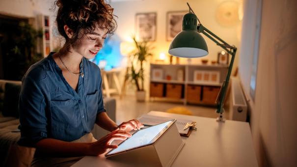 
		Frau sitzt zuhause am Schreibtisch am Tablet
	